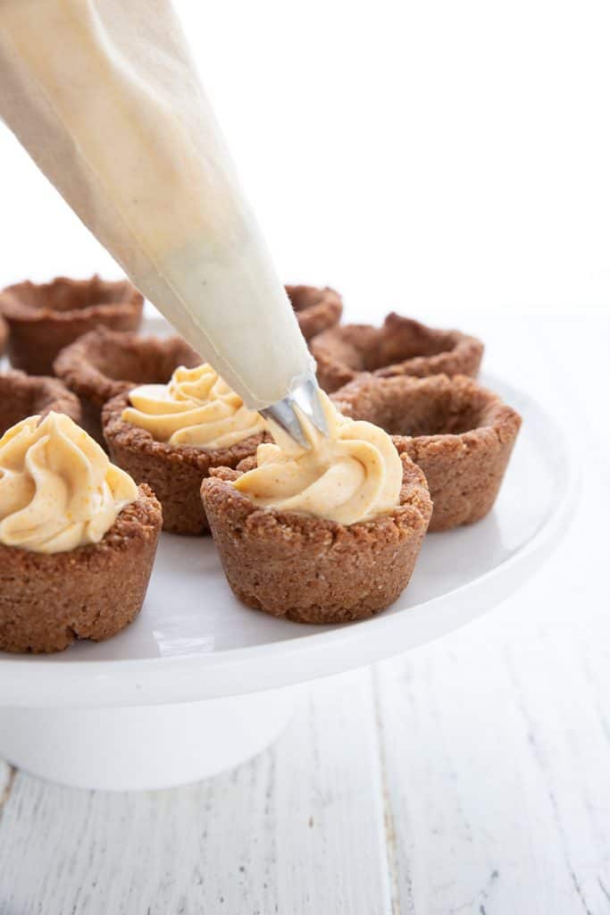 A piping bag piping keto pumpkin cheesecake mousse into a mini cookie cup.