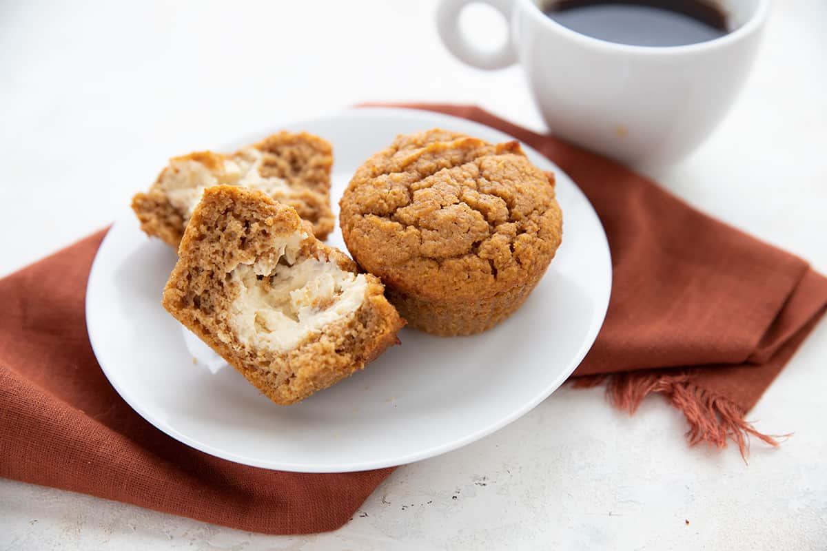 Two keto pumpkin muffins on a white plate with a cup of coffee behind. 