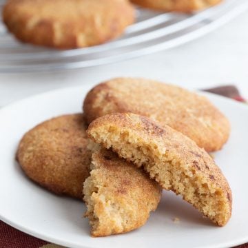 Keto snickerdoodles on a white plate with one broken open to show the inside.