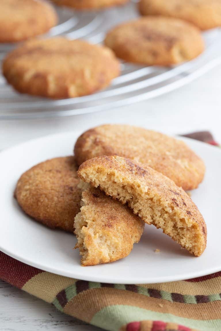 Keto snickerdoodles on a white plate with one broken open to show the inside.