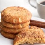 Keto snickerdoodles in a stack on a white plate with one broken open in front.