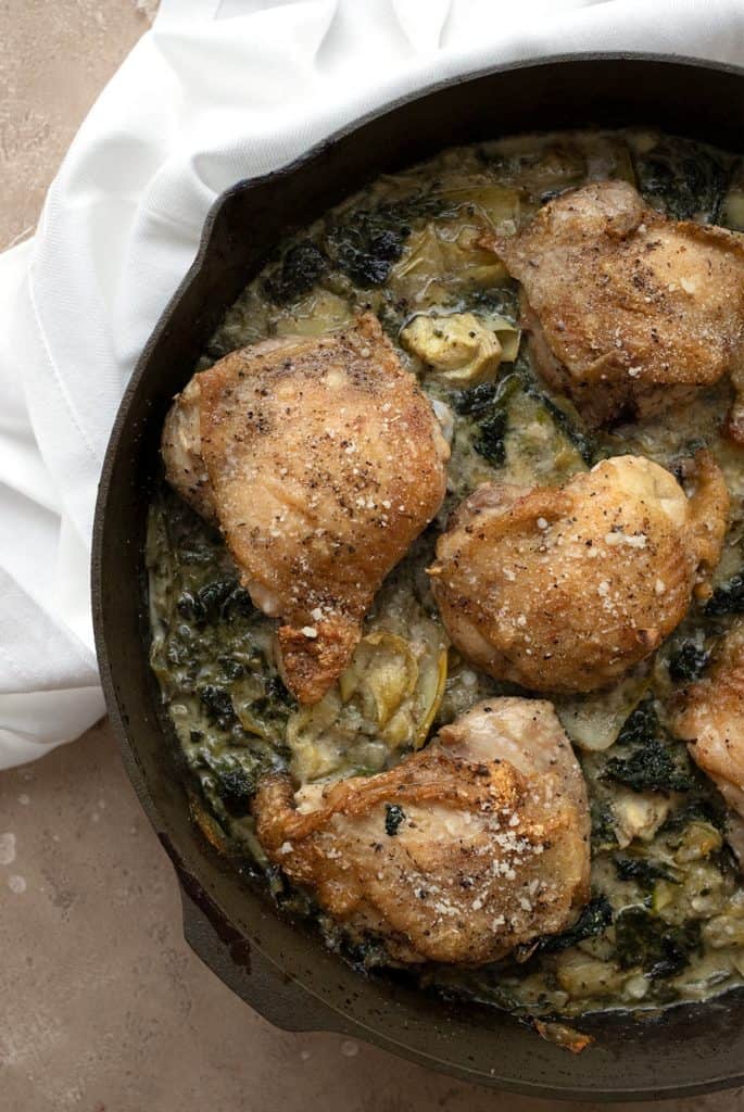 Top down image of crispy chicken thighs over a bed of spinach artichoke sauce.