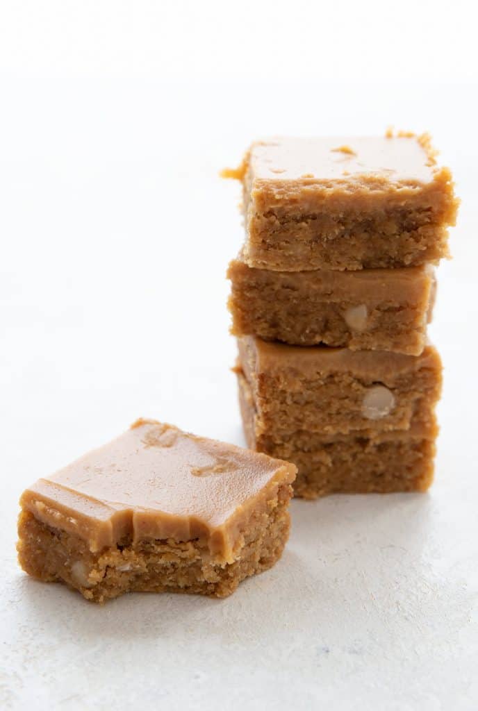 A keto peanut butter blondie with a bite taken out of it, in front of a stack of other blondies.