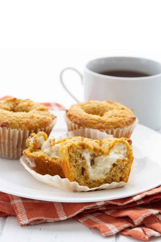 Keto pumpkin muffins on a white plate with a cup of coffee in the background.