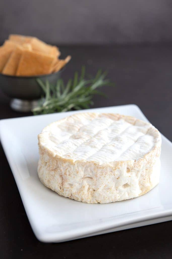A small round of brie on a white plate, prior to baking.