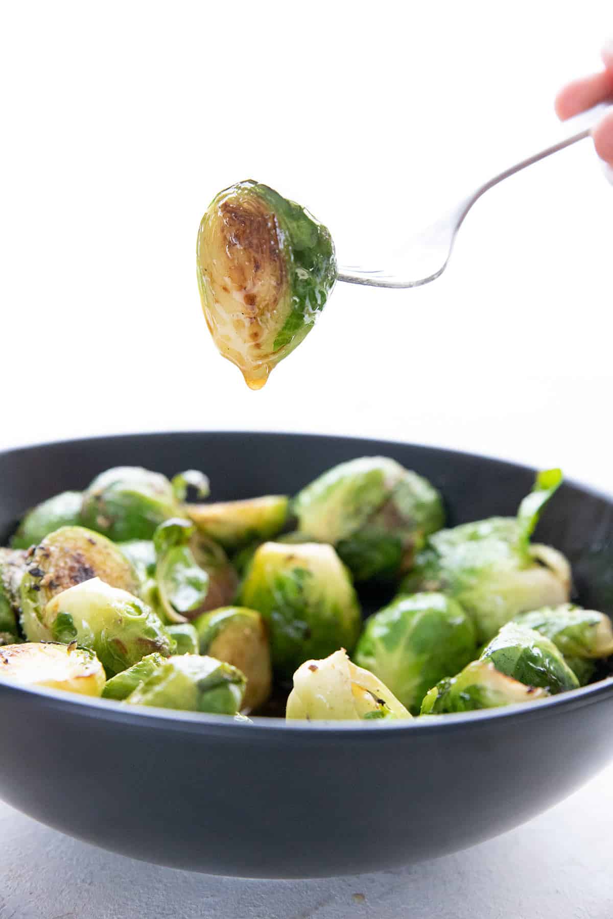 A fork holds up a caramelized brussels sprout dripping with brown butter.