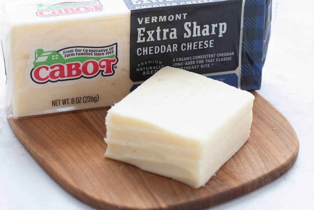 A wooden cutting board with Cabot Extra Sharp on top.