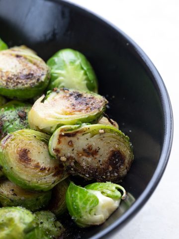 Close up shot of caramelized Brussels sprouts in a black bowl.