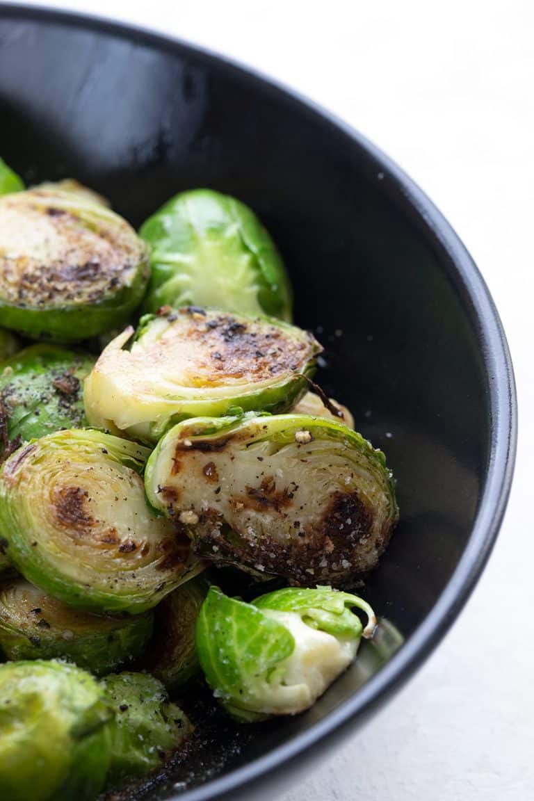 Close up shot of caramelized Brussels sprouts in a black bowl.