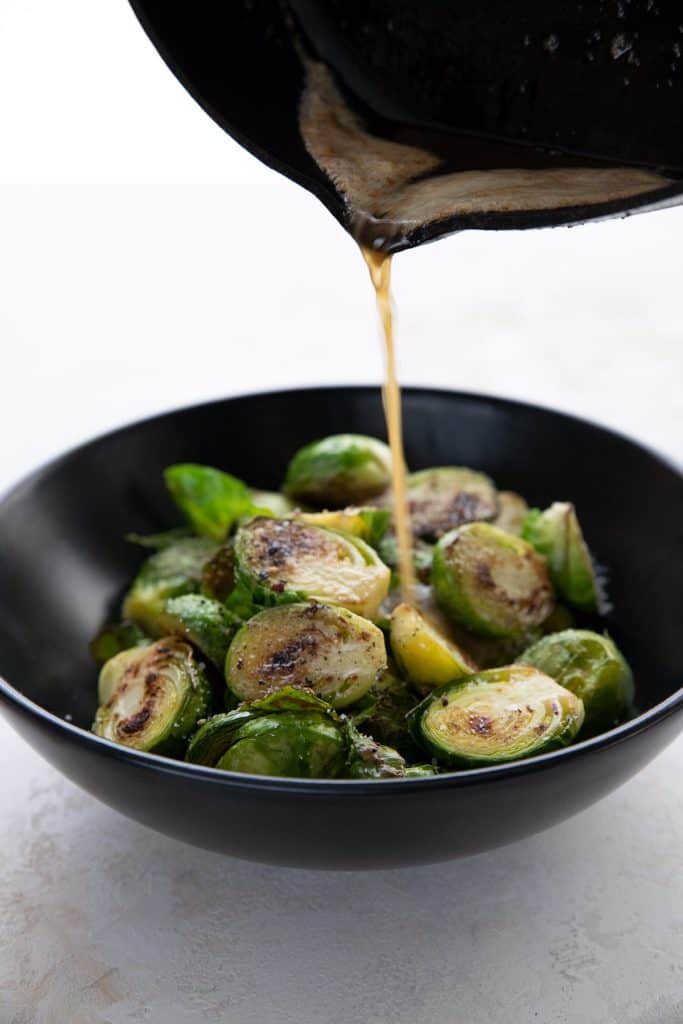 Pouring brown butter over a bowl of caramelized Brussel sprouts.