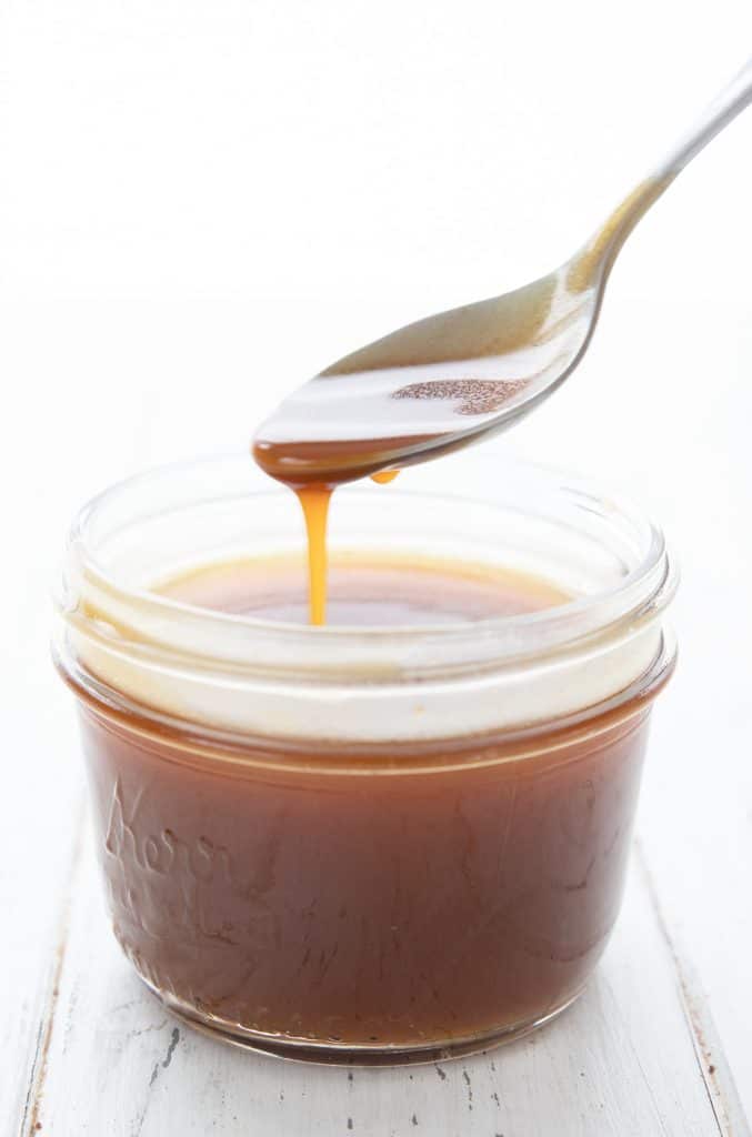 Chewy keto caramel being drizzled off a spoon into a jar.