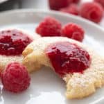 Close up shot of a keto jam thumbprint cookie on a white plate with raspberries in the background.
