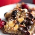 Titled image of two Cranberry Pecan Keto Magic Bars on a white plate with a red ribbon in the background.