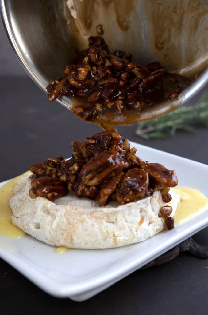 Pouring keto pecan praline sauce over a plate of baked brie.