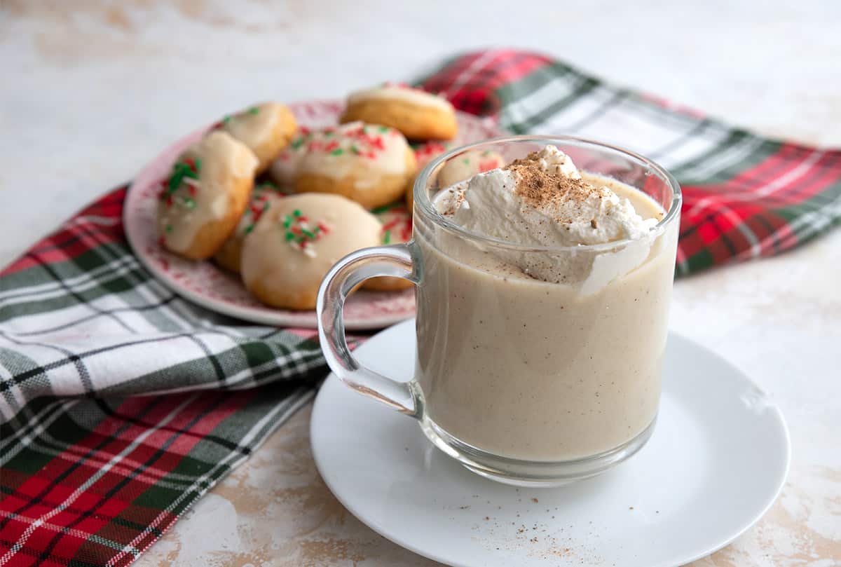 A glass of keto eggnog sits in front of a plate of keto holiday cookies over a plaid napkin.