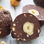 Titled image of homemade keto Ferrero Rocher on a white table with one cut open.