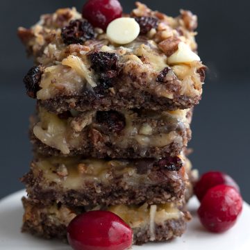 A stack of keto cranberry magic bars on a white cake stand.