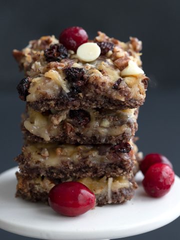 A stack of keto cranberry magic bars on a white cake stand.