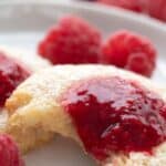 Titled image of a Keto Jam Thumbprint Cookie on a white plate with a bite taken out of it.