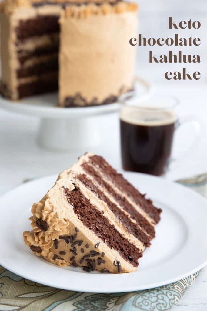 A slice of keto kahlua cake on a white plate in front of the cake on a cake stand.