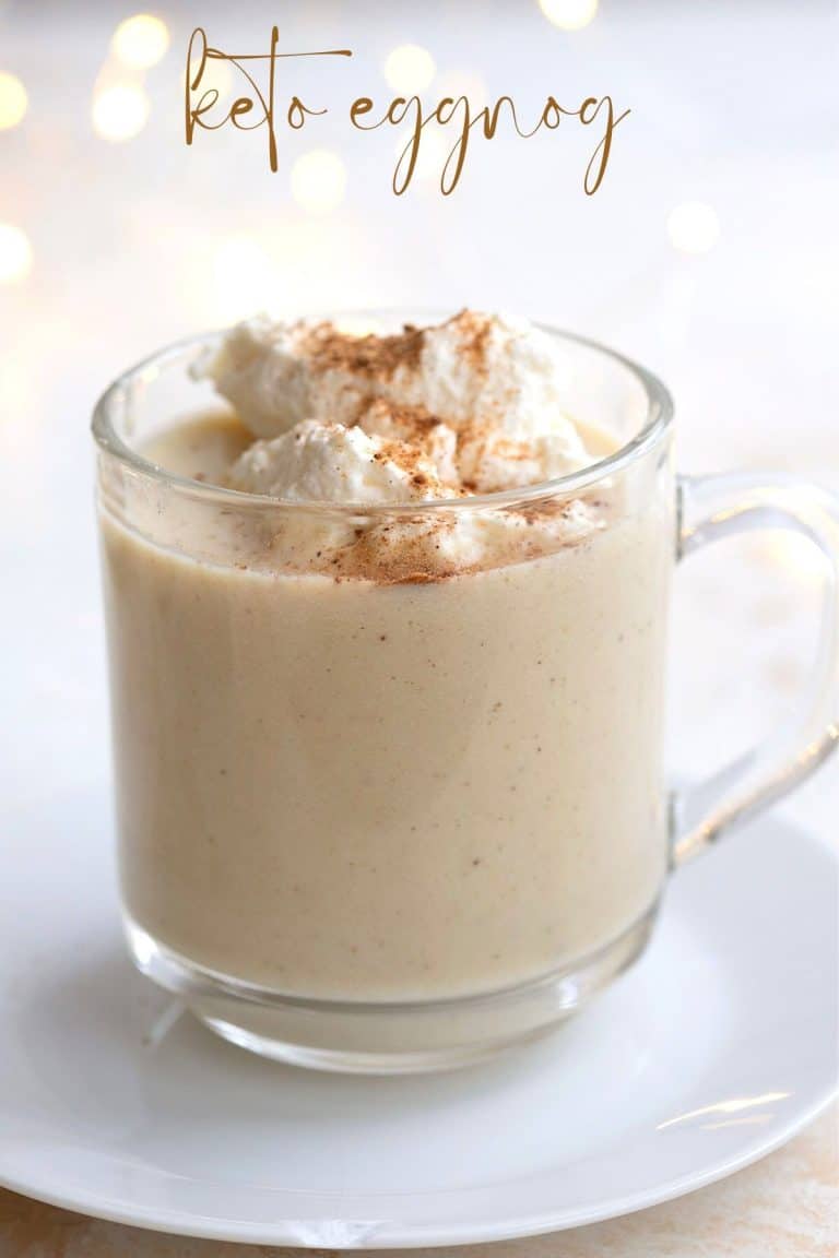 A glass of keto eggnog on a white plate with whipped cream on top.