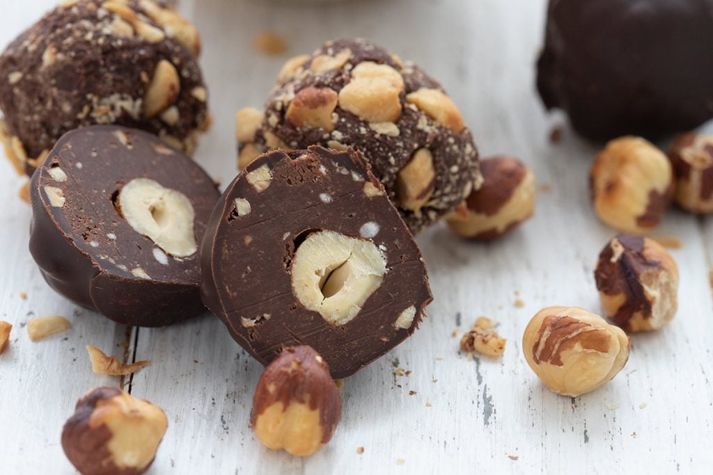 Close up shot of keto chocolate hazelnut truffles with hazelnuts scattered around.