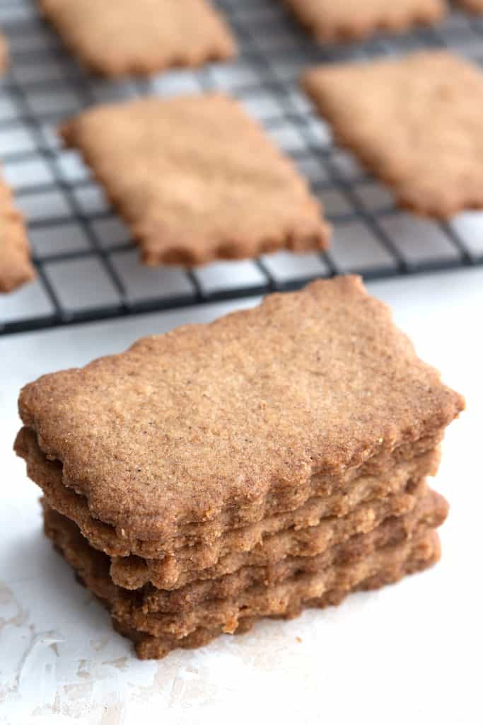 A stack of keto spice cookies with more cookies on a cooling rack in the background.