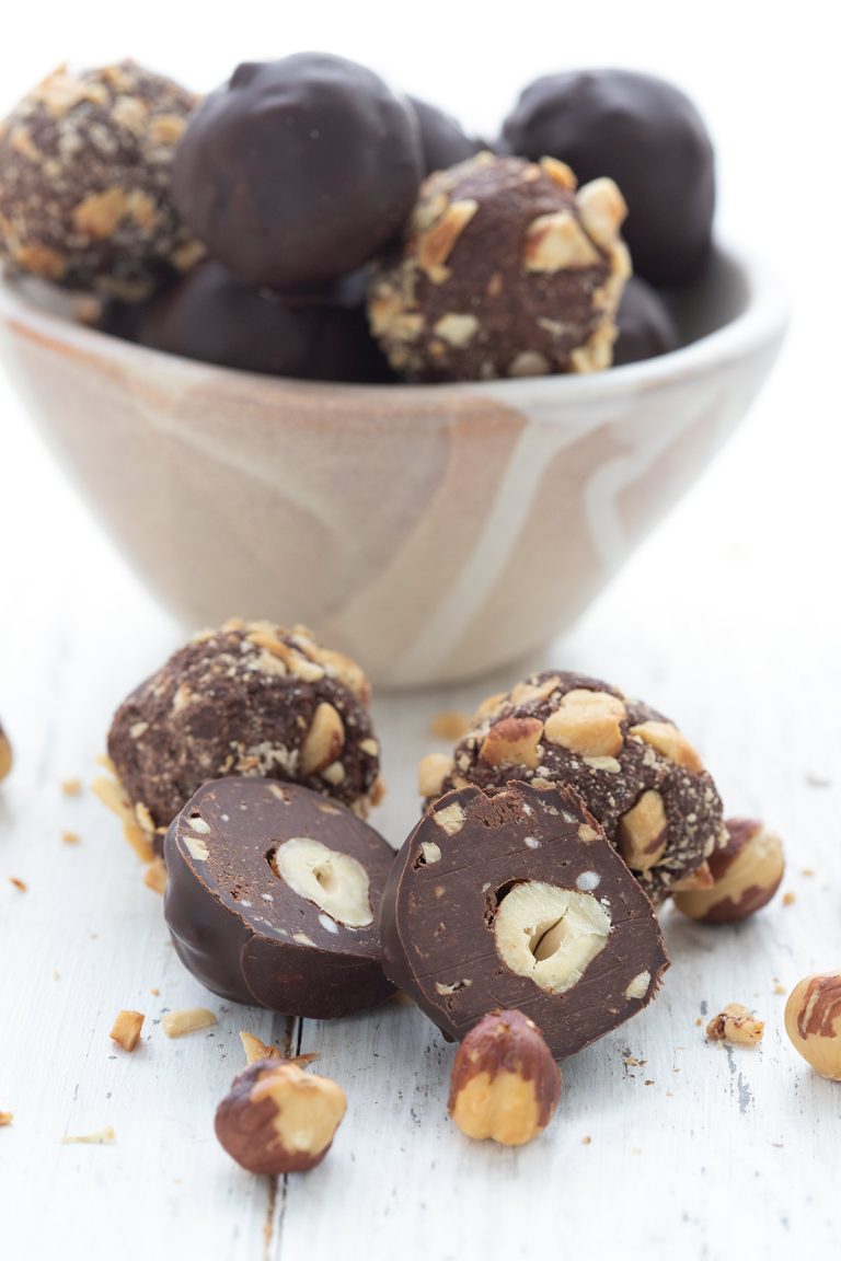 A keto Ferrero Rocher truffle sliced open to show the hazelnut inside, in front of a bowl of more truffles.