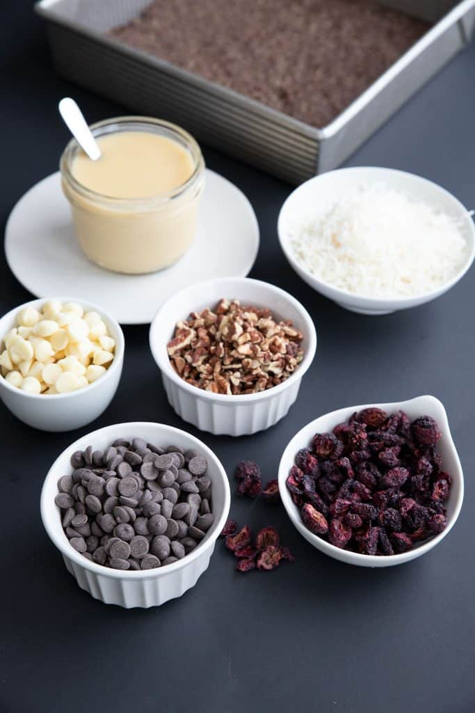 The ingredients for keto holiday magic bars in white bowls on a black background.