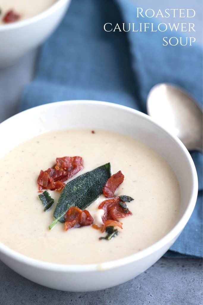 A bowl of roasted cauliflower soup with a crispy sage leaf and prosciutto on top.