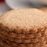 A stack of crispy Keto Speculoos Cookies on a white table with a cup of coffee in the background.