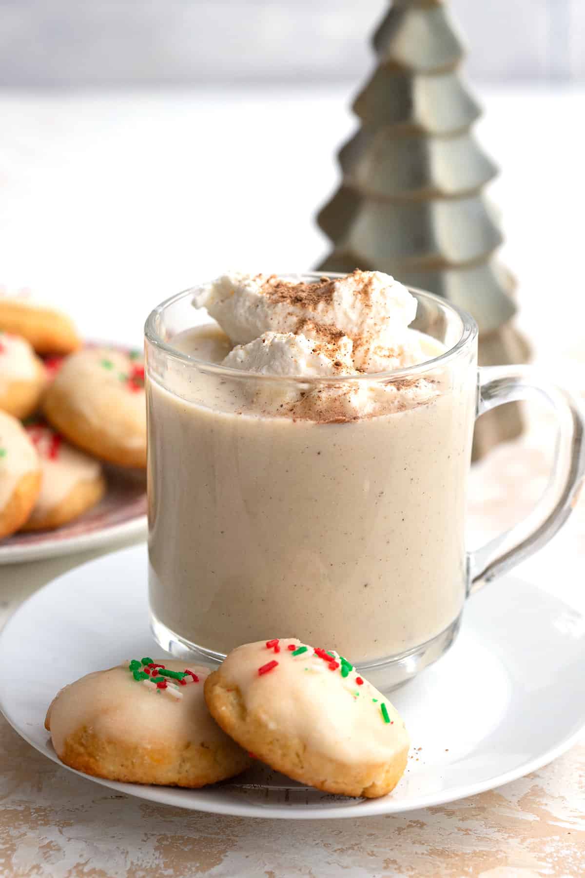 A glass mug filled with keto eggnog on a white plate with two keto cookies.