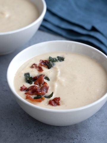 Close up shot of roasted cauliflower soup with crispy prosciutto and sage on top.