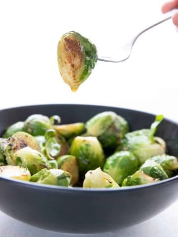 A fork holds up a caramelized brussels sprout dripping with brown butter.
