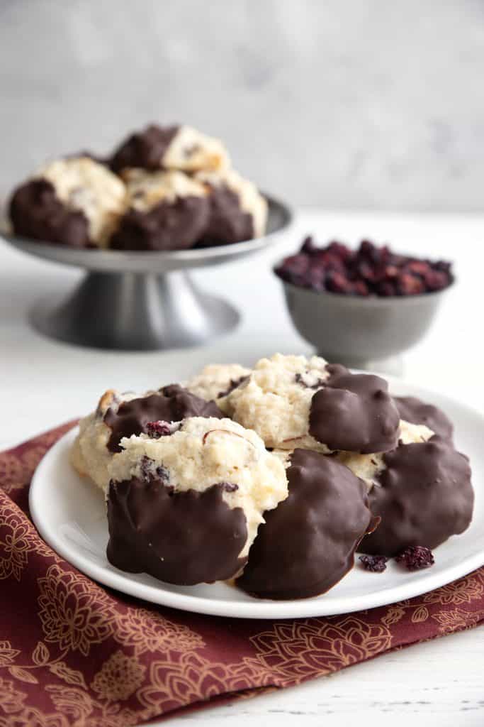 Chocolate dipped keto macaroons on a white plate over a maroon and gold patterned napkin.
