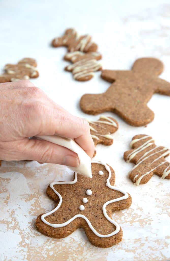 A hand piping sugar-free royal icing over keto gingerbread cookies.