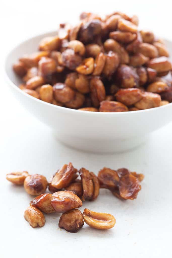 Sugar free toffee peanuts in a small pile with a white bowl of peanuts in the background.