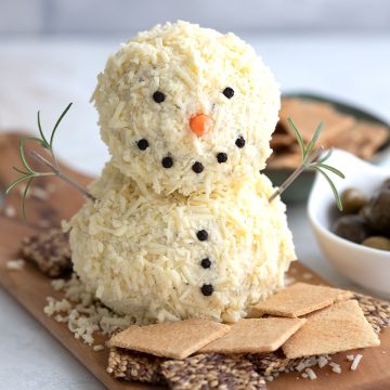 A snowman shaped cheeseball on a platter surrounded by crackers.