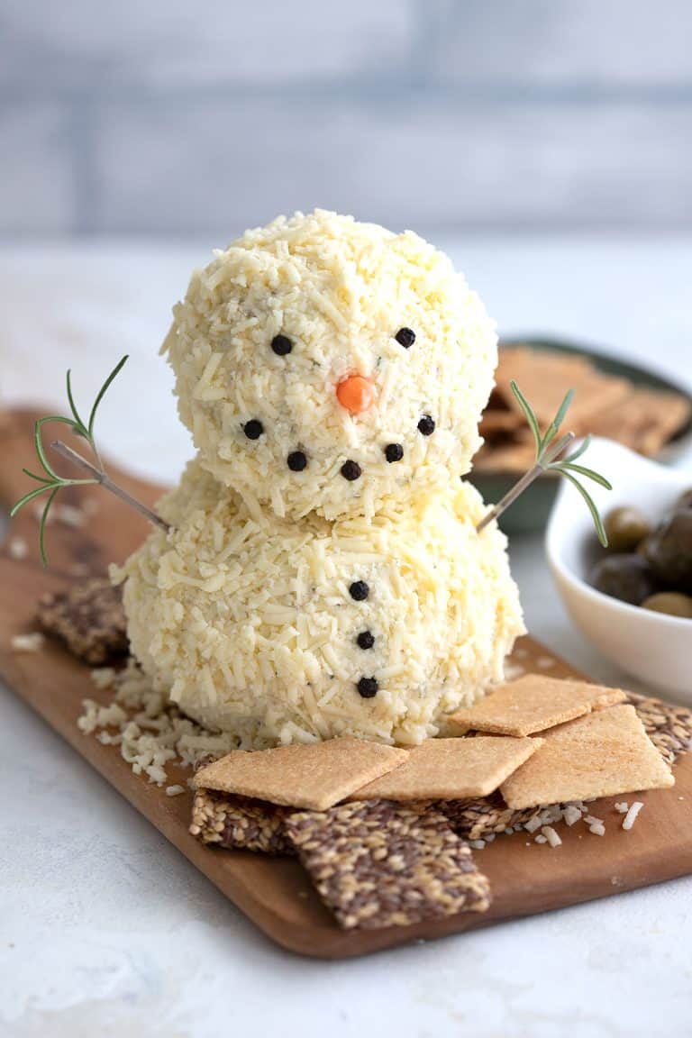 A snowman shaped cheeseball on a platter surrounded by crackers.