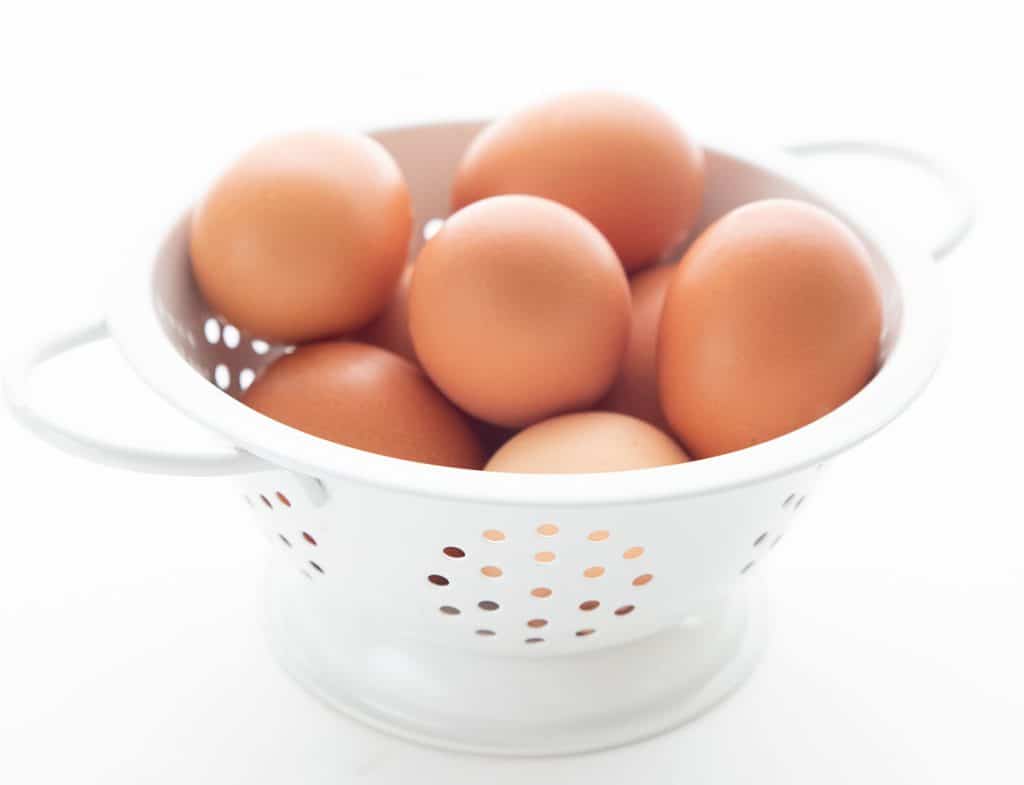 A white colander filled with eggs.