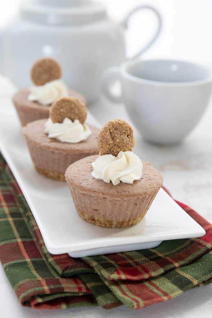 Three mini keto cheesecakes on a white tray over a green and red plaid napkin.