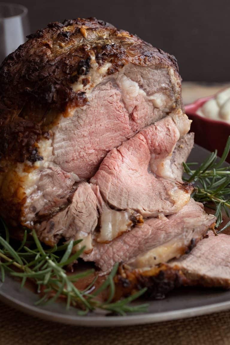 A standing rib roast on a metal platter with several slices carved off in front.