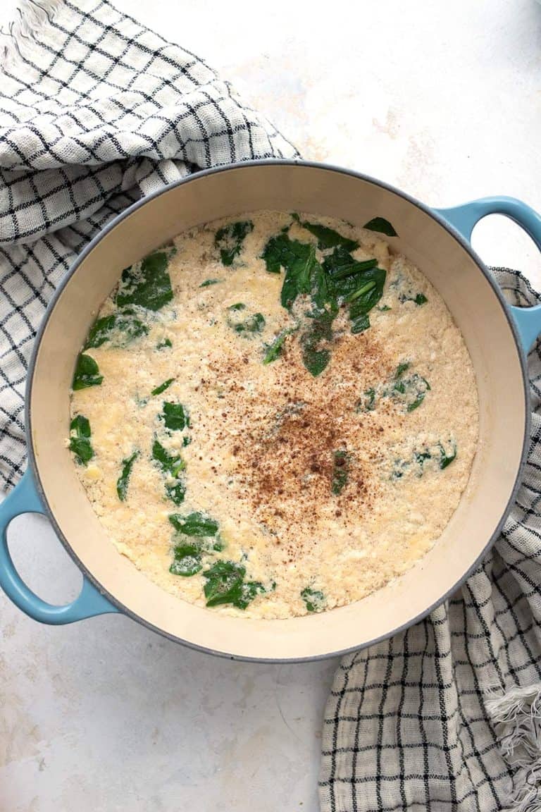 Top down image of stracciatella soup in a blue Dutch oven over a checked tea towel.