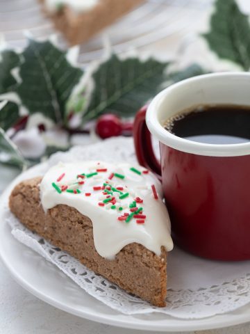 A keto almond flour gingerbread scone sits on a plate with a cup of coffee.
