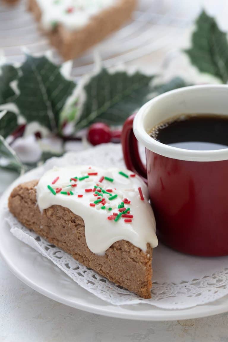 A keto almond flour gingerbread scone sits on a plate with a cup of coffee.