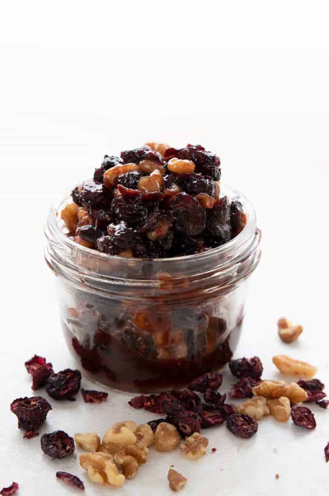 A jar of sugar-free mincemeat on a white background with dried cranberries and walnuts strewn around.