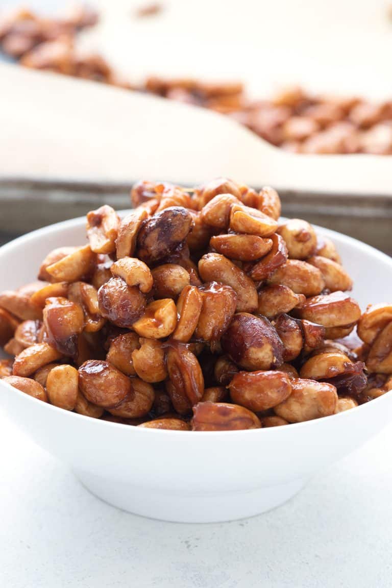 Keto butter toffee peanuts in a white bowl with the pan in the background.