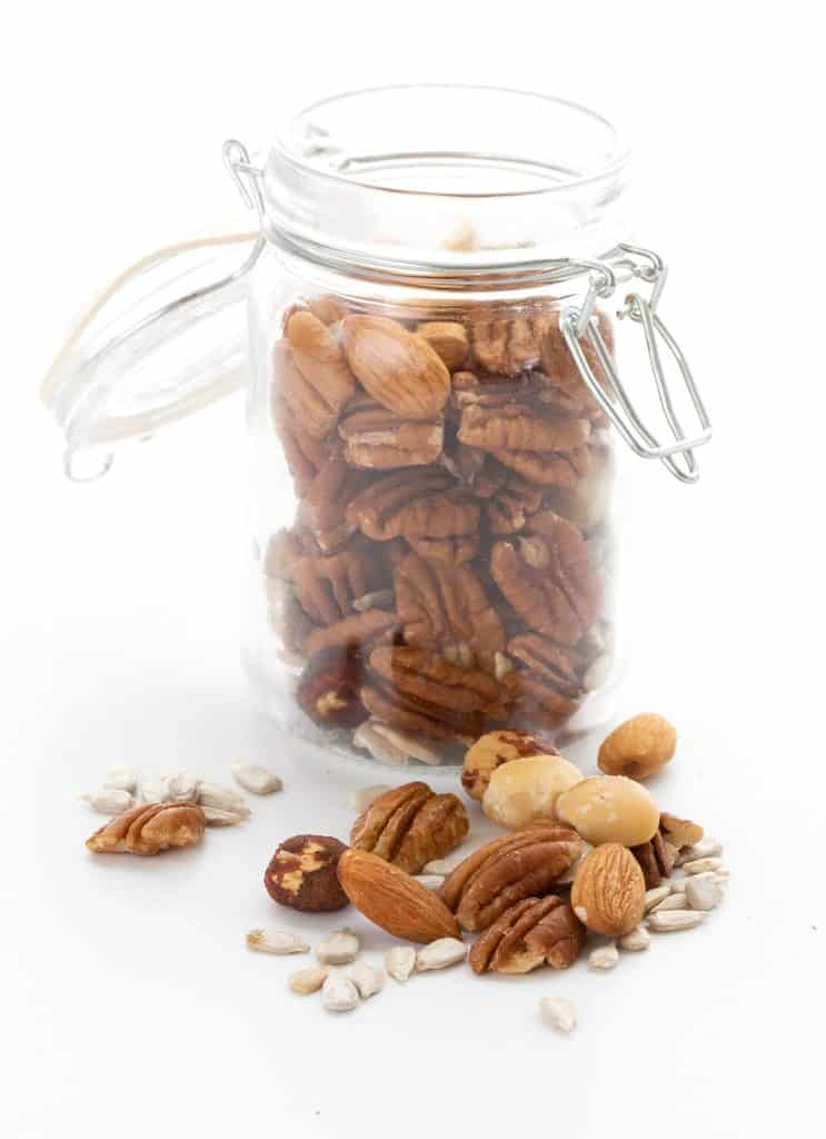 A jar filled with mixed nuts, with more nuts in the foreground.