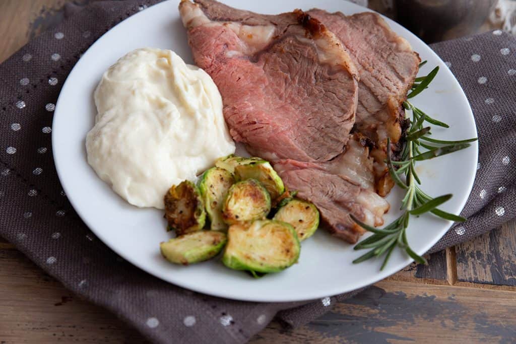 A white plate with prime rib, Brussels sprouts and mashed cauliflower.
