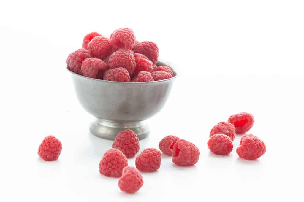 A metal bowl of raspberries on a white background.